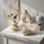 Matte white swirl vase with dried stems, arch vase on a riser and fan vase on its side on a white console