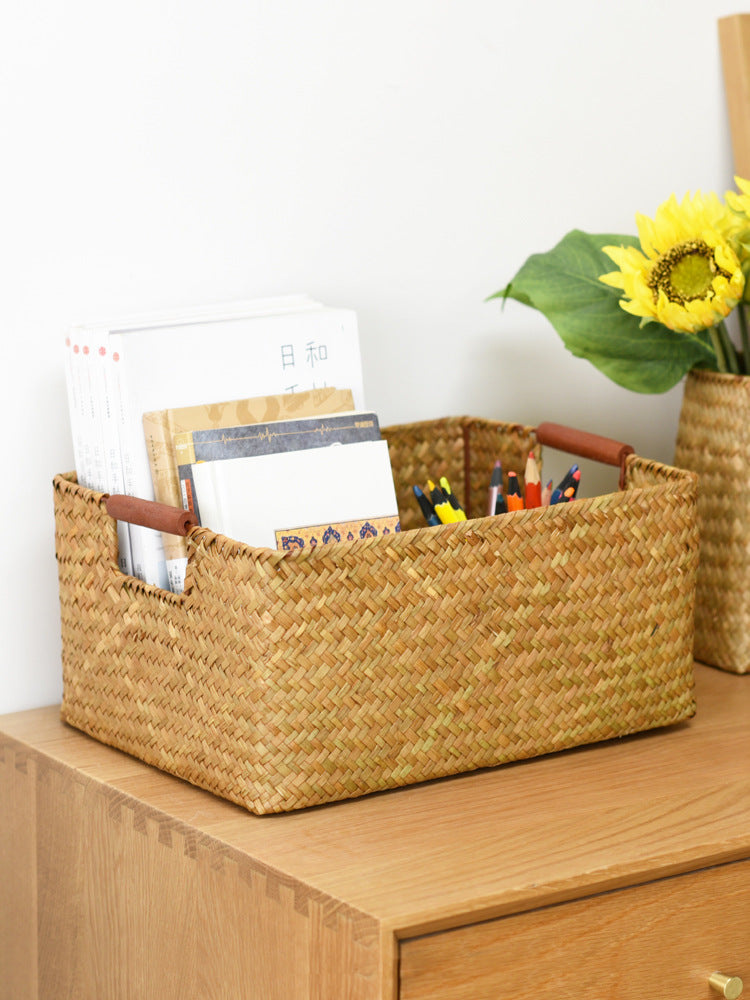 Seagrass storage basket with wooden handles holding books and pencils on an oak nightstand