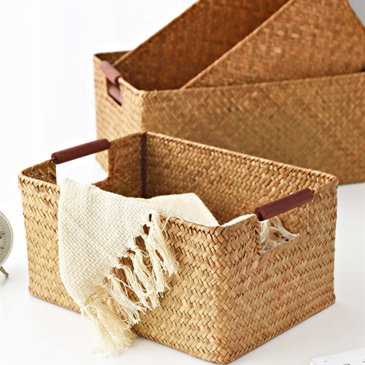 Seagrass storage basket with wooden handle bars holding a cream fringed throw, on a white surface