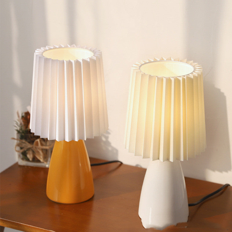Burnt orange and white pleated ceramic lamps lit side by side on a wooden table