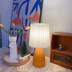 Burnt orange ceramic lamp with pleated shade lit on a lace cloth beside tulips