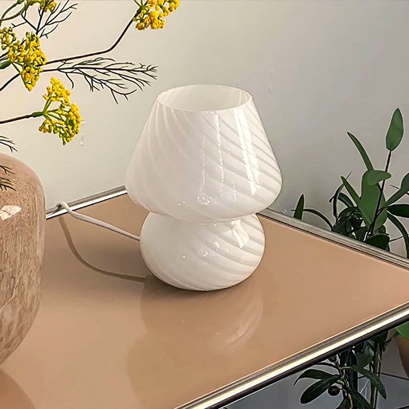 White swirl glass mushroom table lamp on a mirrored side table with yellow flowers