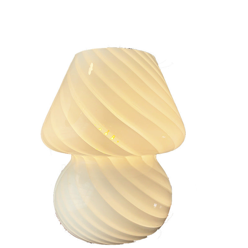 Swirl glass mushroom table lamp, lit, on a plain white background