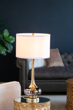 Smoked glass gourd table lamp lit on a gold side table in a navy living room