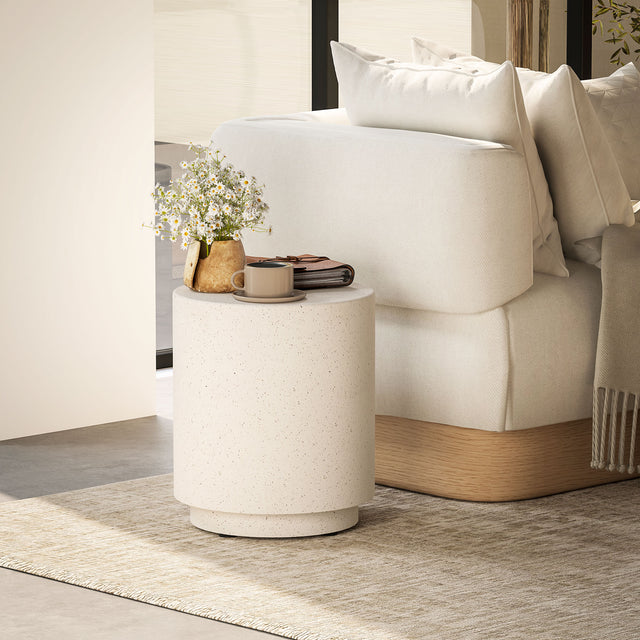 Speckled concrete-look drum side table in cream beside a white sofa, holding daisies, a mug and a journal