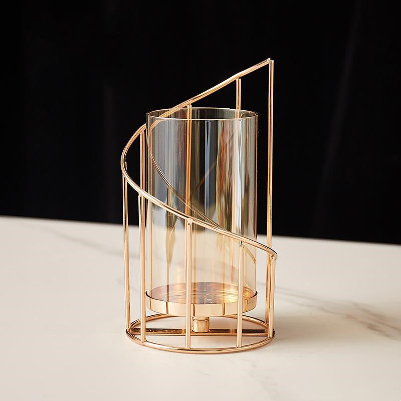 Tall spiral gold-tone hurricane candle holder with amber-tinted glass on white marble, dark backdrop