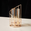 Tall spiral gold-tone hurricane candle holder with amber-tinted glass on white marble, dark backdrop