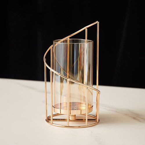 Tall spiral gold-tone hurricane candle holder with amber-tinted glass on white marble, dark backdrop