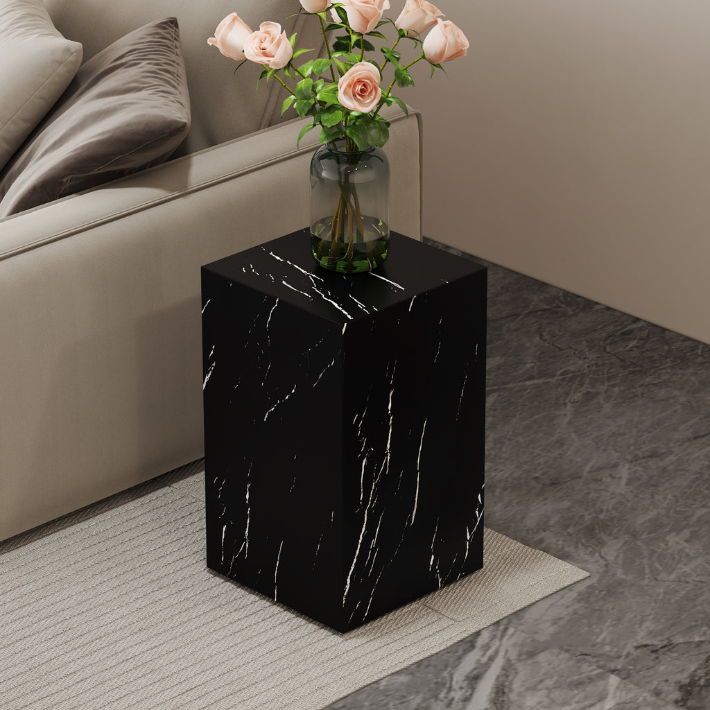 Black faux marble pedestal side table holding a vase of pink roses beside a cream sofa