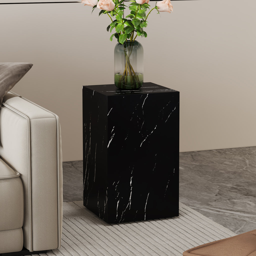Square faux marble side table with roses in a glass vase next to a sofa arm on a grey floor