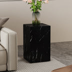 Square faux marble side table with roses in a glass vase next to a sofa arm on a grey floor