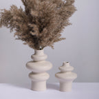 Three ring and two ring stacked ceramic vases in speckled cream, the taller holding dried pampas grass