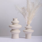 Three ring and two ring stacked ceramic vases in speckled cream, the shorter holding white dried pampas