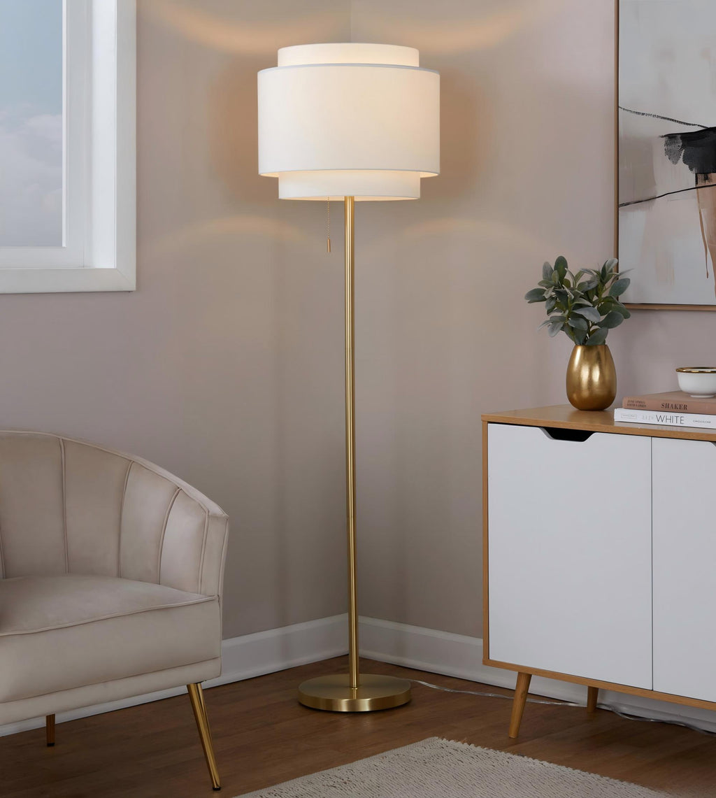 Tiered linen shade floor lamp lit in a living room corner beside a velvet armchair and white sideboard