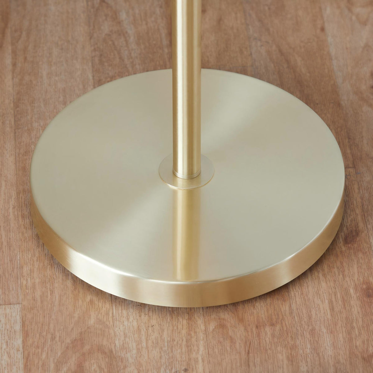 Tiered linen shade floor lamp — detail of the flat round gold base on a wood floor