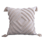 Square cream tufted pillow cover, concentric diamond pattern, corner tassels, on a white background