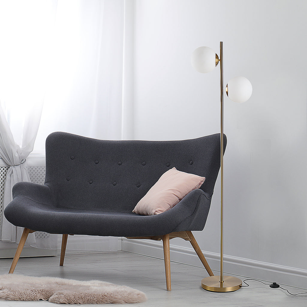 Gold twin globe floor lamp beside a charcoal loveseat with a pink pillow in a pale gray room
