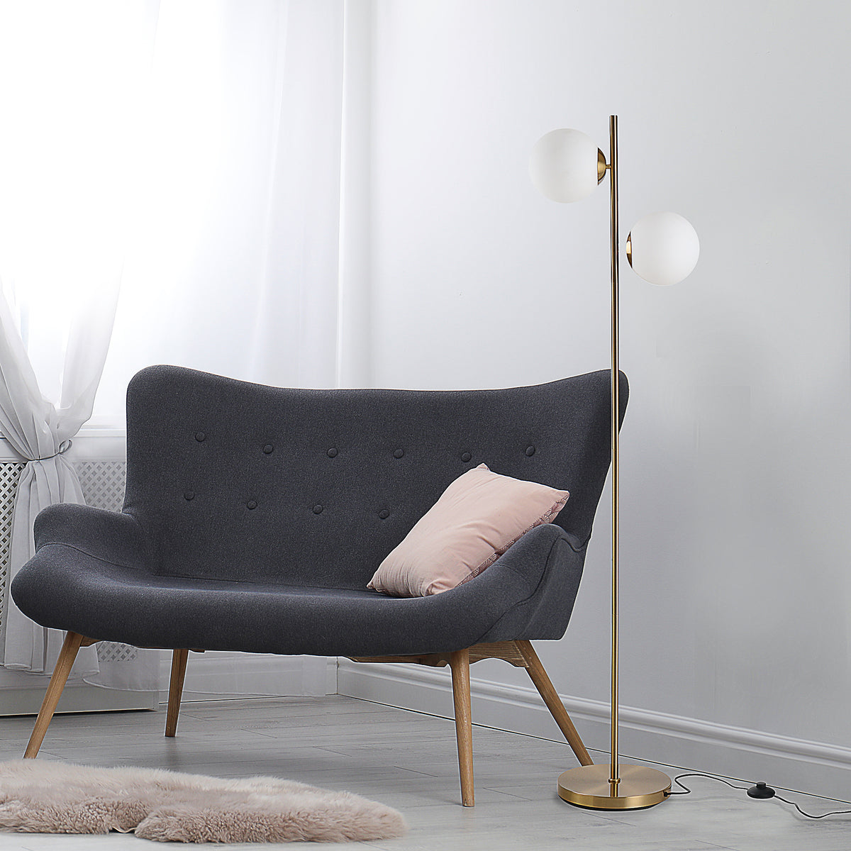 Gold twin globe floor lamp beside a charcoal loveseat with a pink pillow in a pale gray room