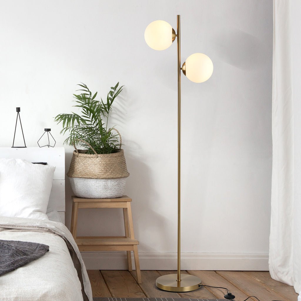 Twin globe floor lamp in gold beside a bed and a stool holding a woven basket planter