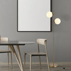 Gold twin globe floor lamp by a dining table and wood chairs against a gray wall