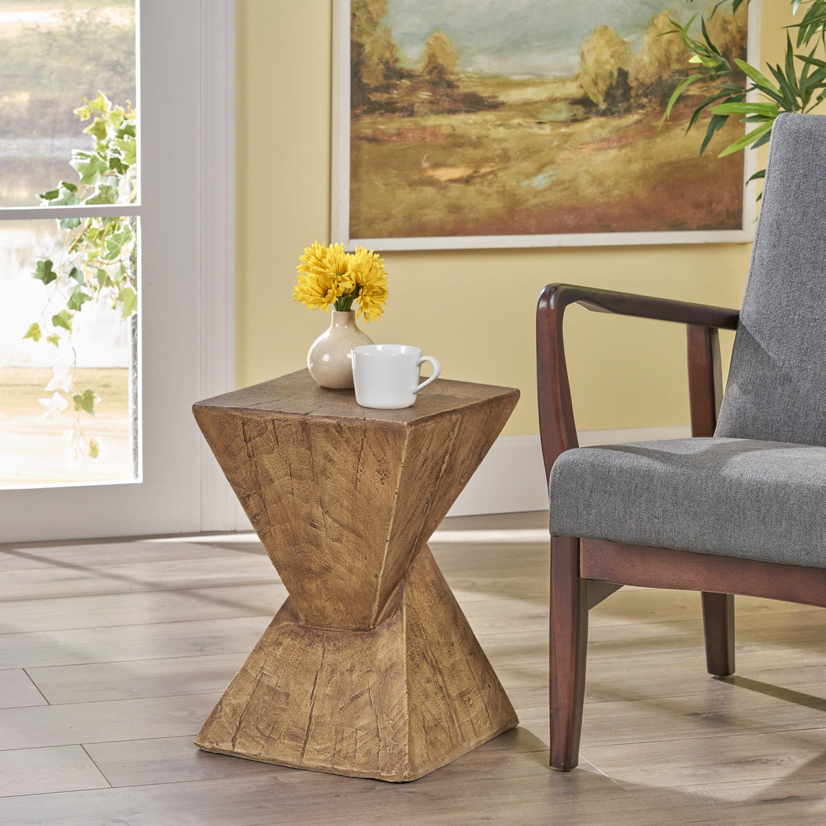 Twisted hourglass side table beside a grey armchair with a mug and yellow flowers on top