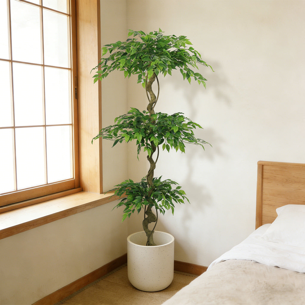 Six-foot faux ficus tree in a white pot in the corner of a sunlit bedroom by a window