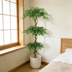 Six-foot faux ficus tree in a white pot in the corner of a sunlit bedroom by a window