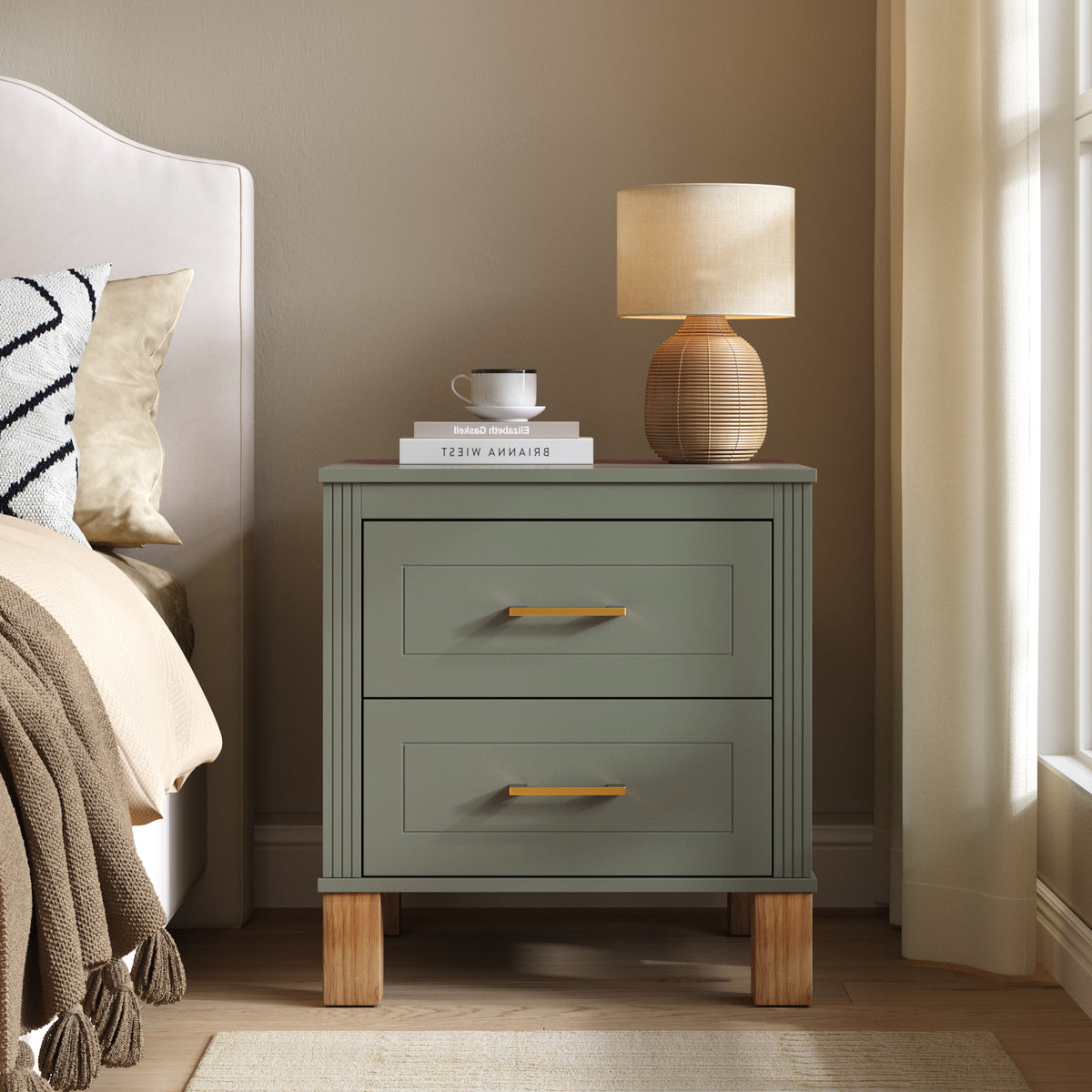 Olive green nightstand beside a bed with a ribbed table lamp, a cup and books