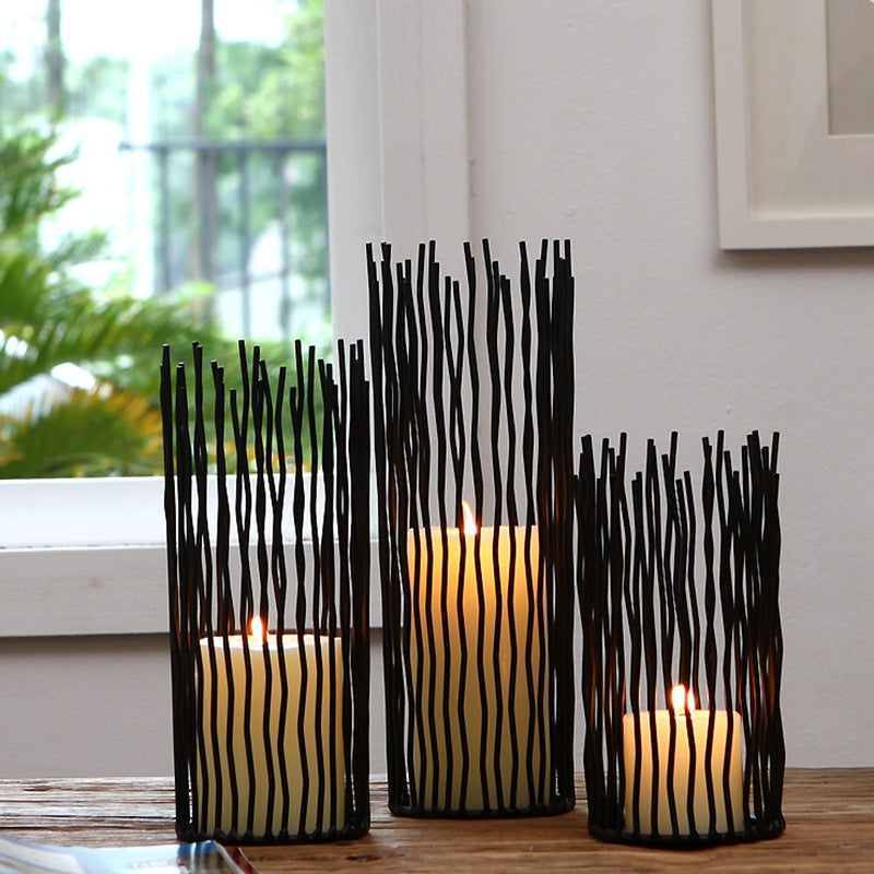 Three black iron rod candle holders glowing with pillar candles on a table by a window