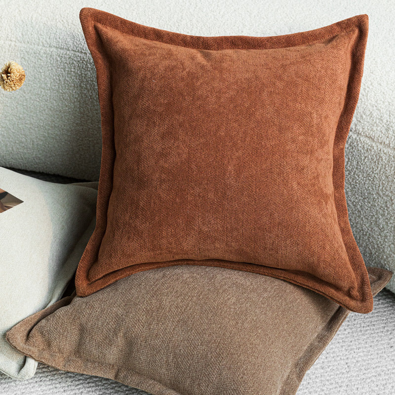 Wide flange-edge chenille pillow cover in rust resting on a coffee one on a cream bouclé sofa