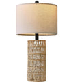 Woven rattan column table lamp with linen-look drum shade, lit, on a plain white background