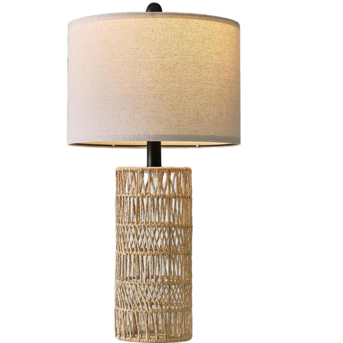 Woven rattan column table lamp with linen-look drum shade, lit, on a plain white background