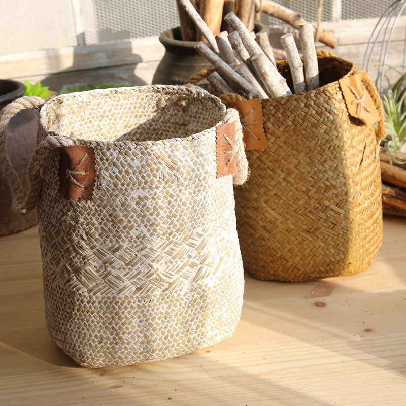Sand and caramel seagrass plant baskets side by side on a wooden table, one holding driftwood