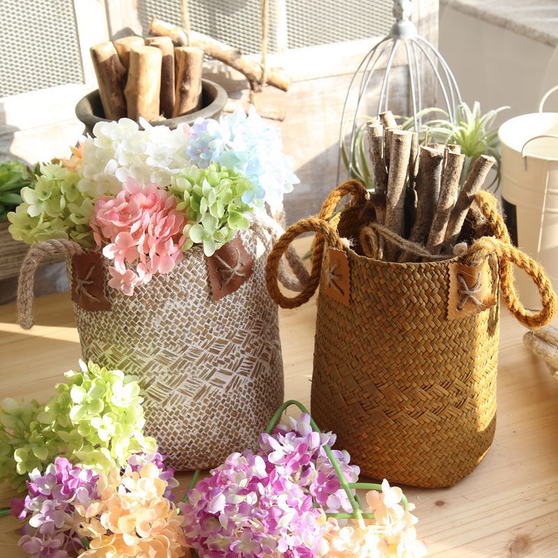Sand seagrass basket holding faux hydrangeas beside a caramel basket of driftwood